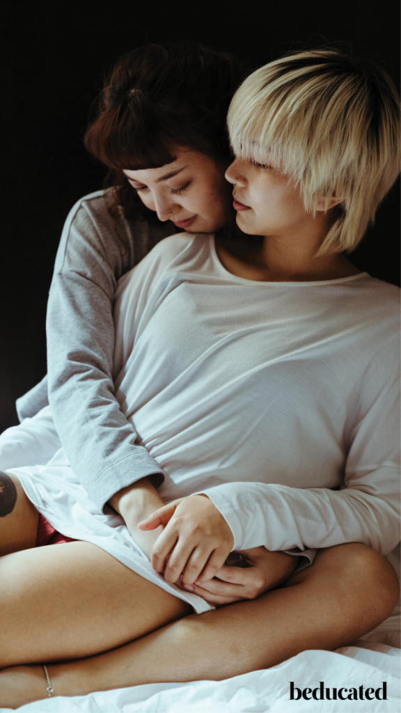 A women in a grey top hugging a woman in a white top from behind.